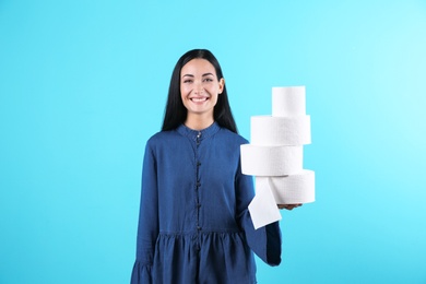 Beautiful woman holding toilet paper rolls on color background