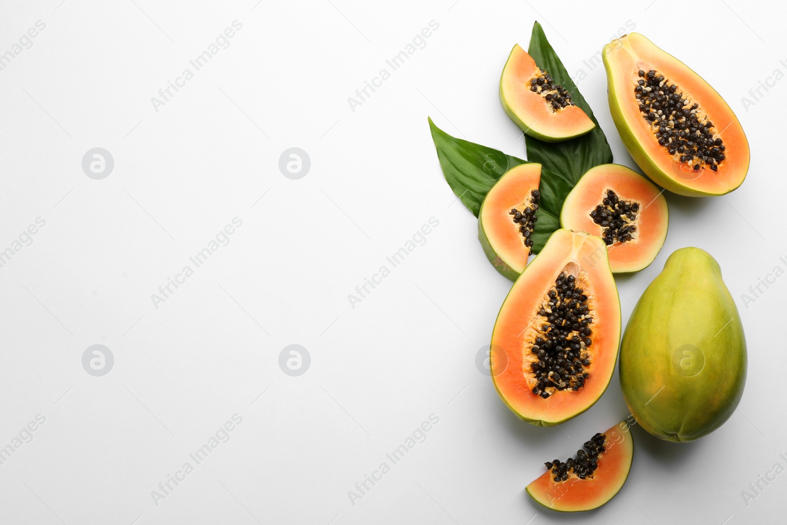 Photo of Fresh ripe papaya fruits with green leaves on white background, flat lay. Space for text