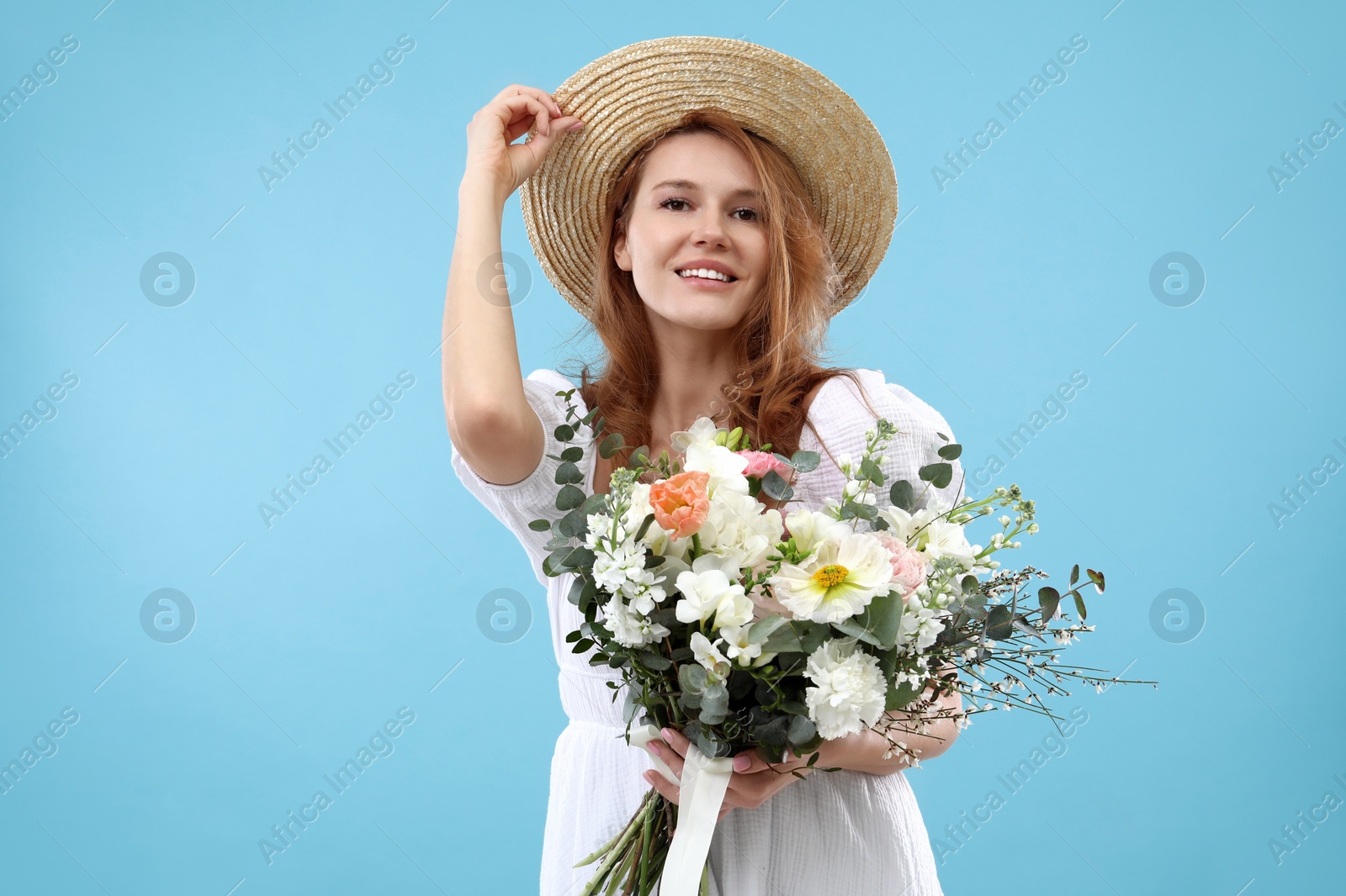 Photo of Beautiful woman in straw hat with bouquet of flowers on light blue background