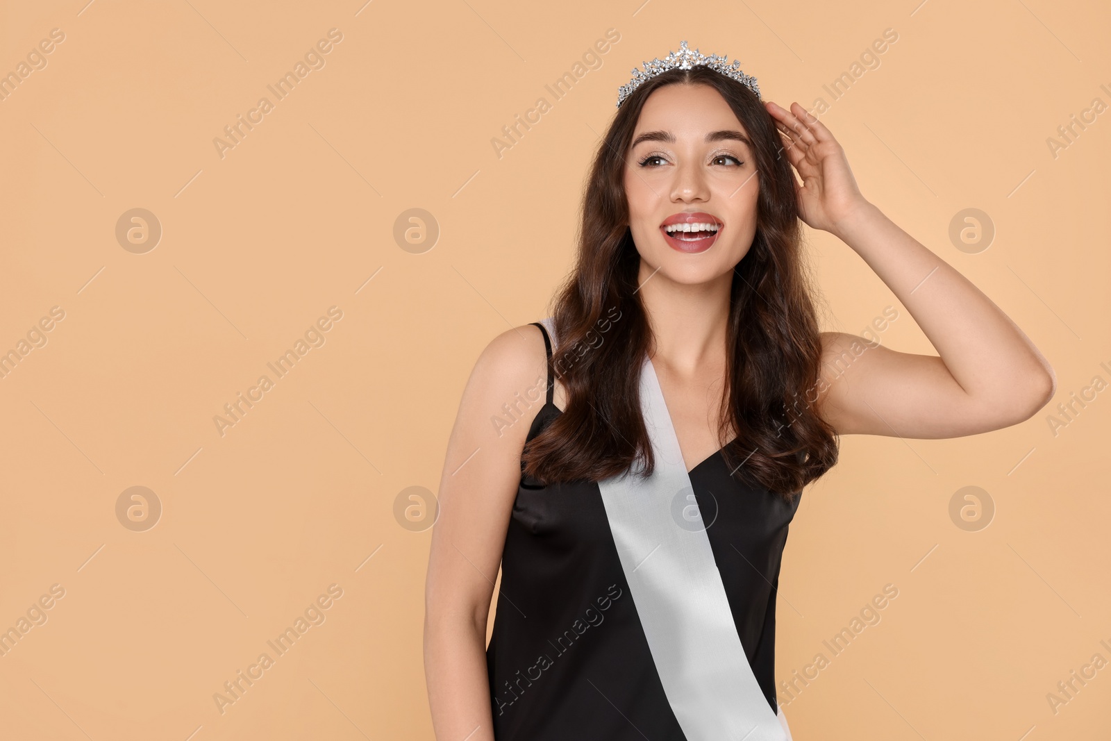 Photo of Beautiful young woman with tiara and ribbon in dress on beige background, space for text. Beauty contest