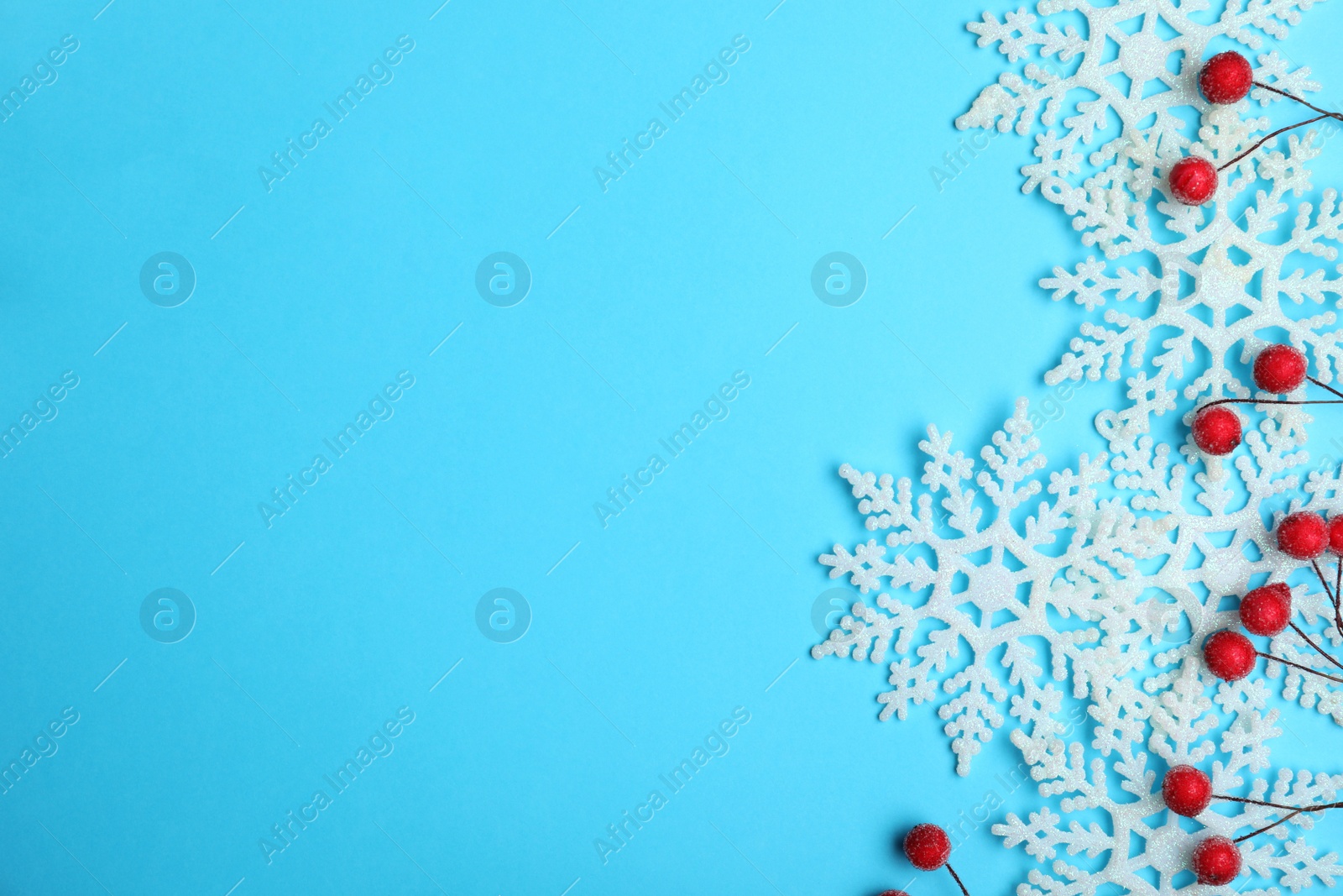 Photo of Beautiful decorative snowflakes and red berries on light blue background, flat lay. Space for text