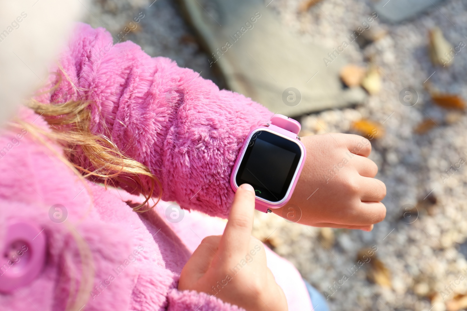 Photo of Little girl using smart watch outdoors, closeup