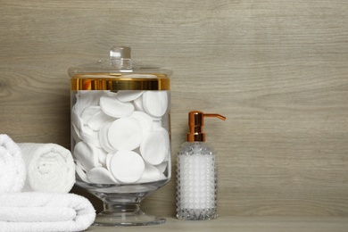 Photo of Composition of glass jar with cotton pads on table near wooden wall. Space for text