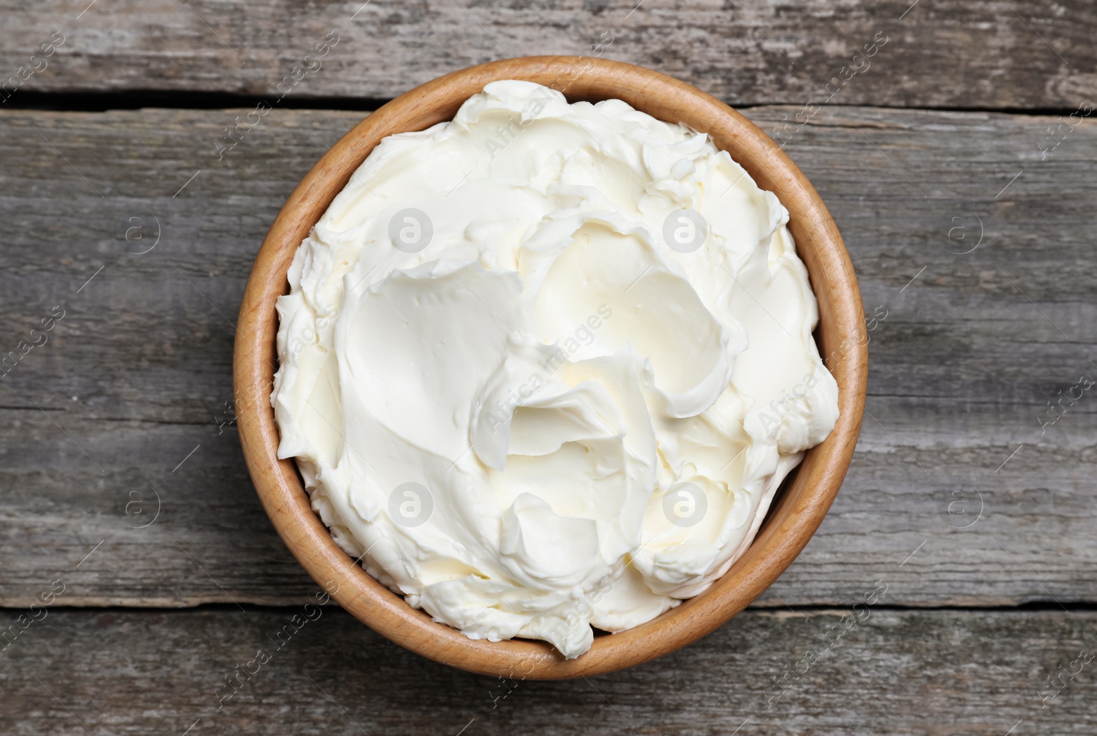 Photo of Bowl of tasty cream cheese on wooden table, top view