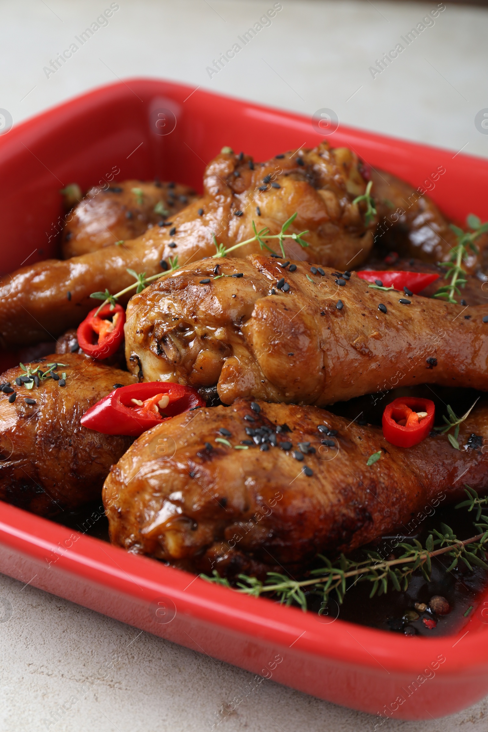 Photo of Chicken legs glazed in soy sauce with black sesame, chili pepper and thyme on light table, closeup