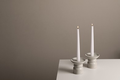 Photo of Holders with burning candles on white table near pale brown wall, space for text