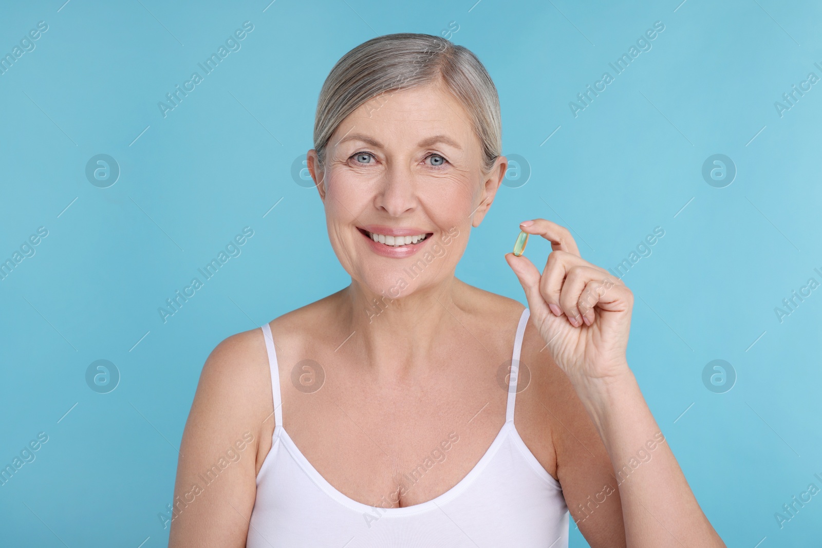 Photo of Beautiful woman with vitamin capsule on light blue background