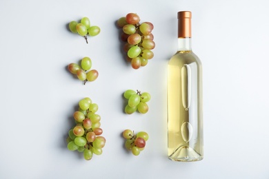 Photo of Bottle with white wine and fresh ripe juicy grapes on light background, top view