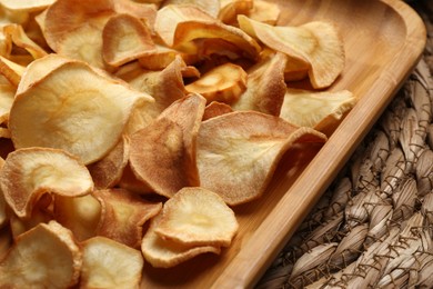 Photo of Tray with tasty homemade parsnip chips on wicker surface, closeup