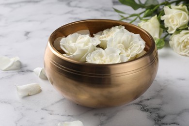Tibetan singing bowl with water and beautiful roses on white marble table, closeup