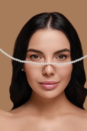 Photo of Young woman with elegant pearl jewelry on brown background, closeup