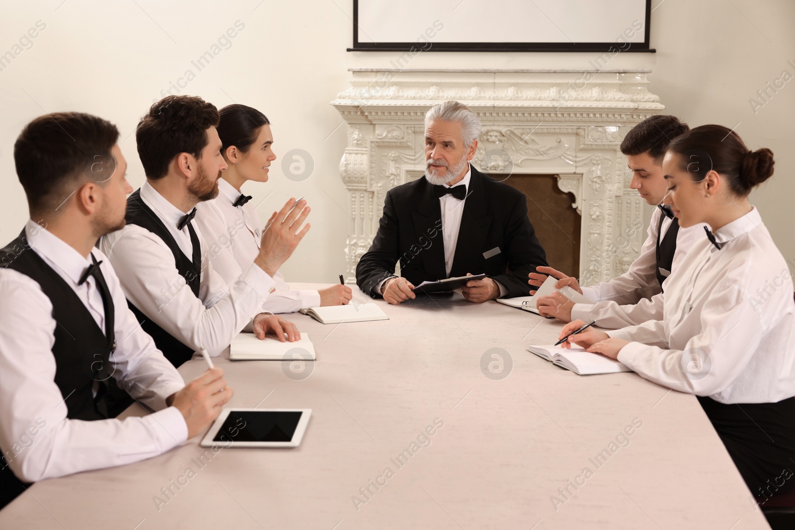 Photo of Senior man in formal suit teaching trainees indoors. Professional butler courses