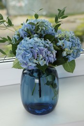 Beautiful blue hortensia flowers in vase on window sill indoors