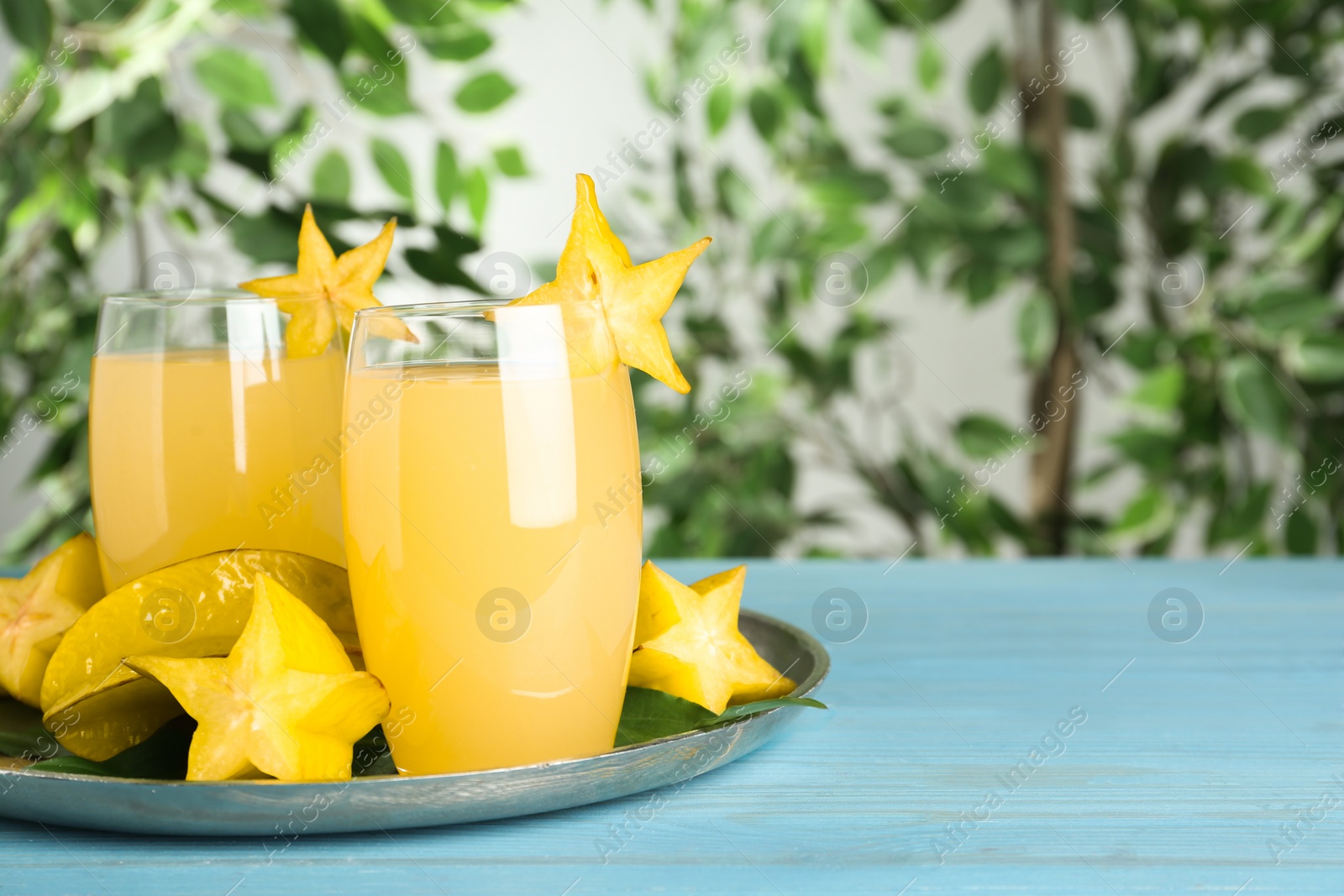 Photo of Delicious carambola juice in glasses on light blue wooden table. Space for text