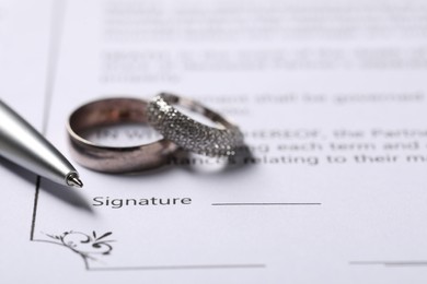 Photo of Marriage contract, pen and wedding rings, closeup