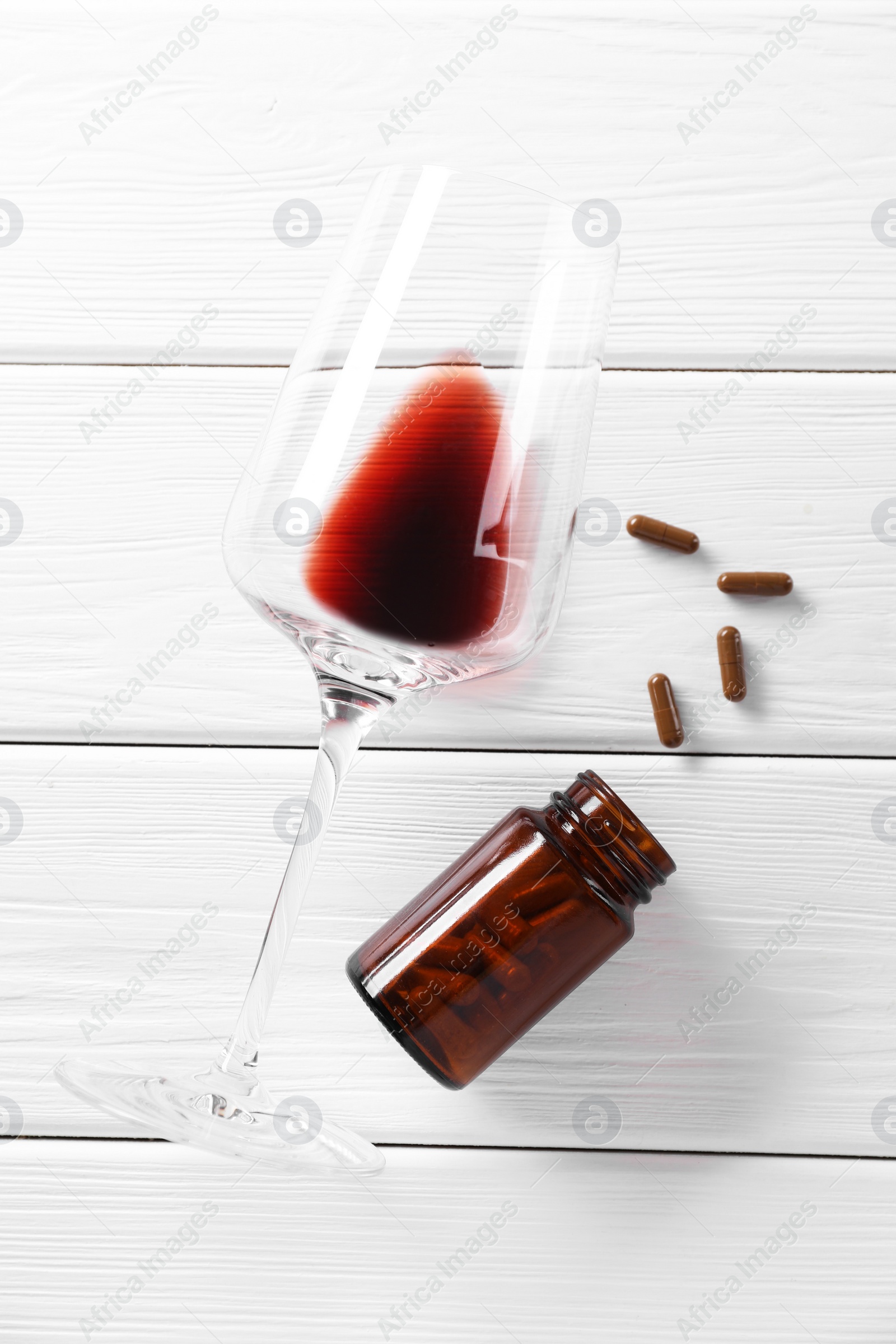 Photo of Alcohol and drug addiction. Glass with red wine, bottle and pills on white wooden table, flat lay