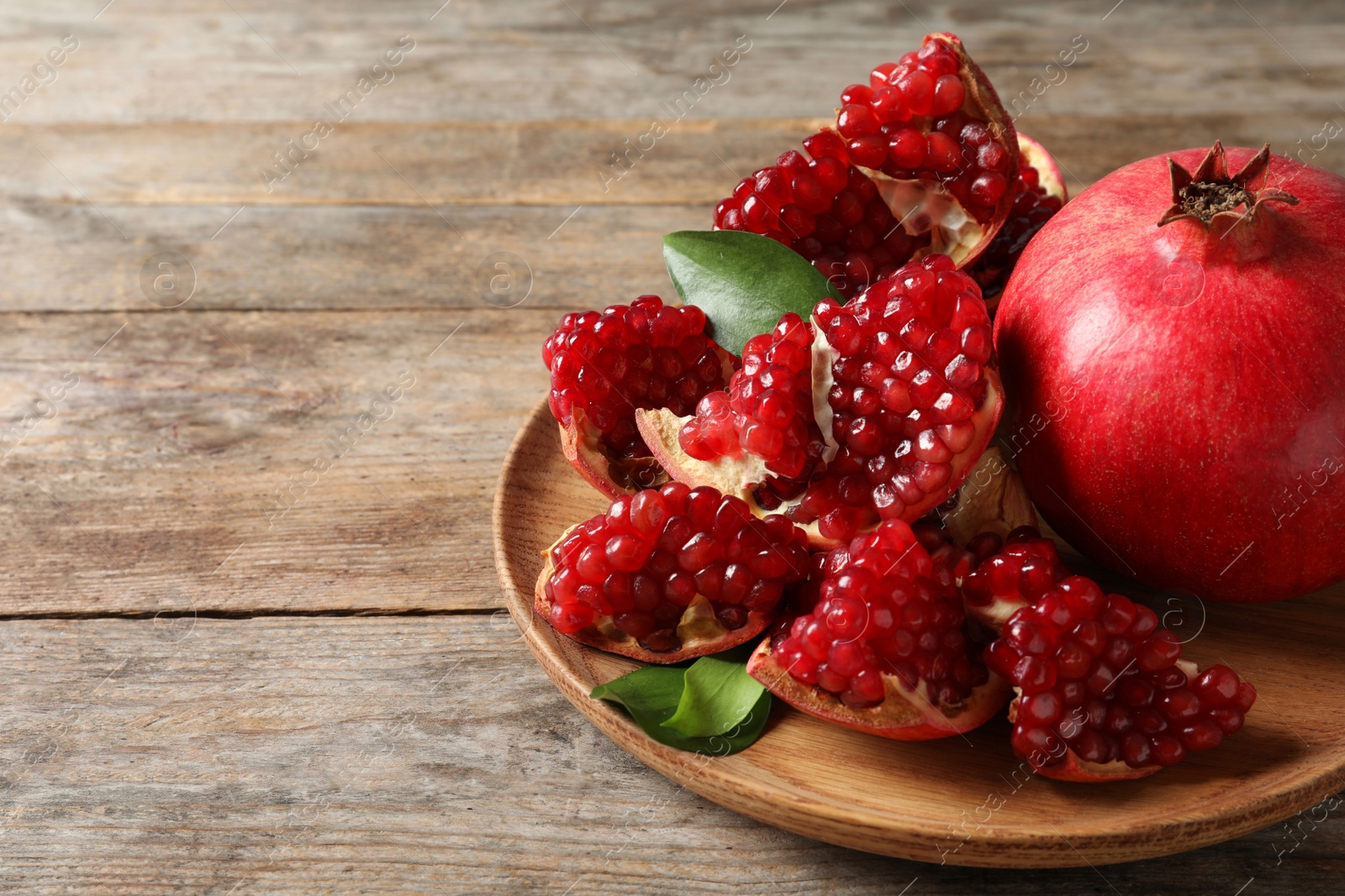 Photo of Plate with ripe pomegranates and seeds on wooden background, space for text