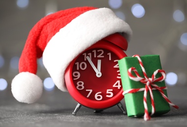 Alarm clock with decor on grey table against blurred Christmas lights, closeup. New Year countdown