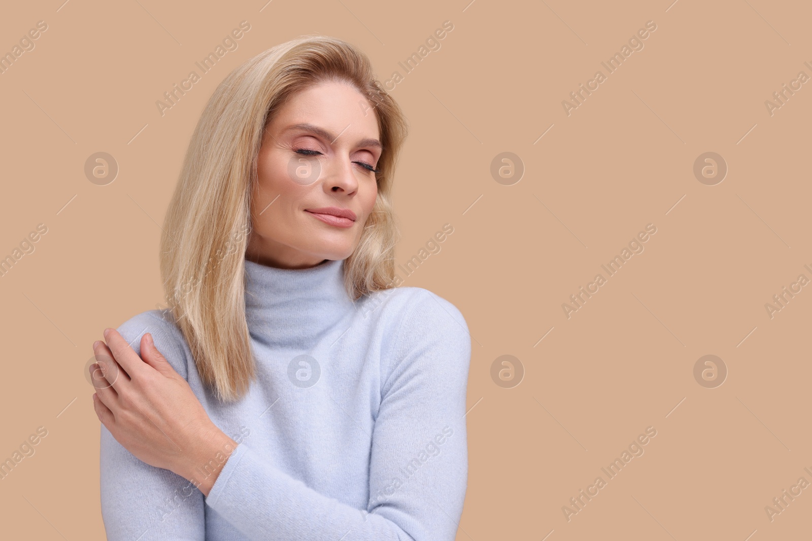 Photo of Portrait of beautiful middle aged woman with blonde hair on beige background. Space for text