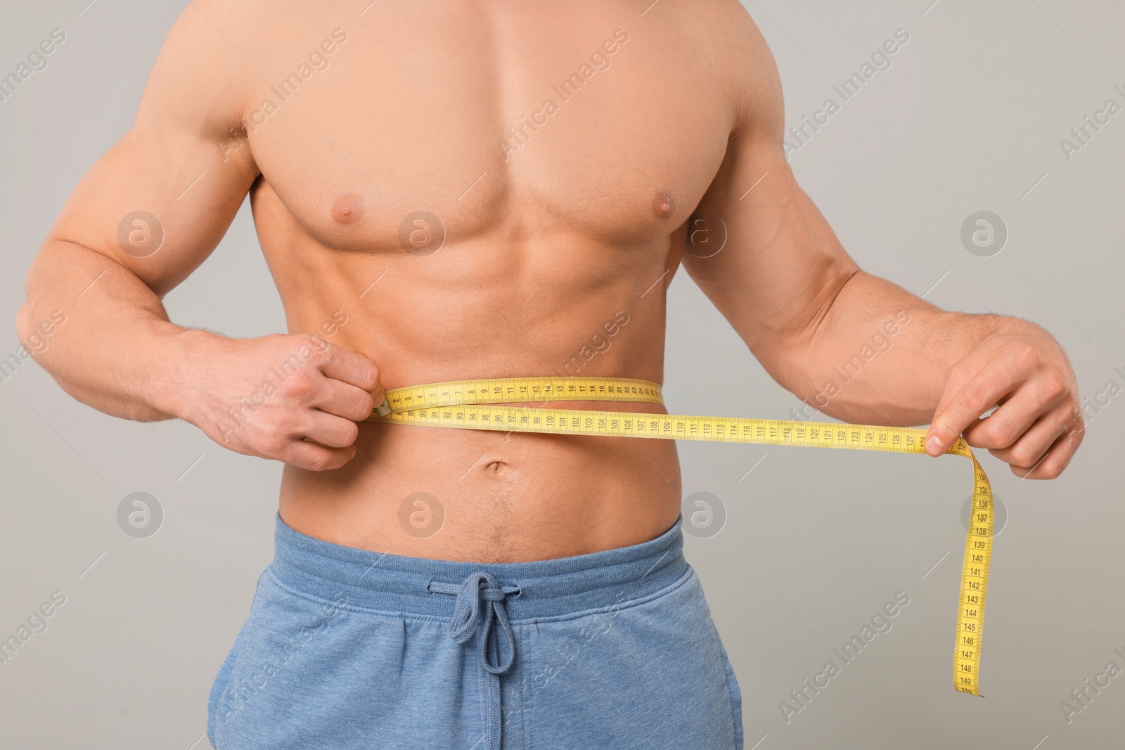 Photo of Athletic man measuring waist with tape on light grey background, closeup. Weight loss concept