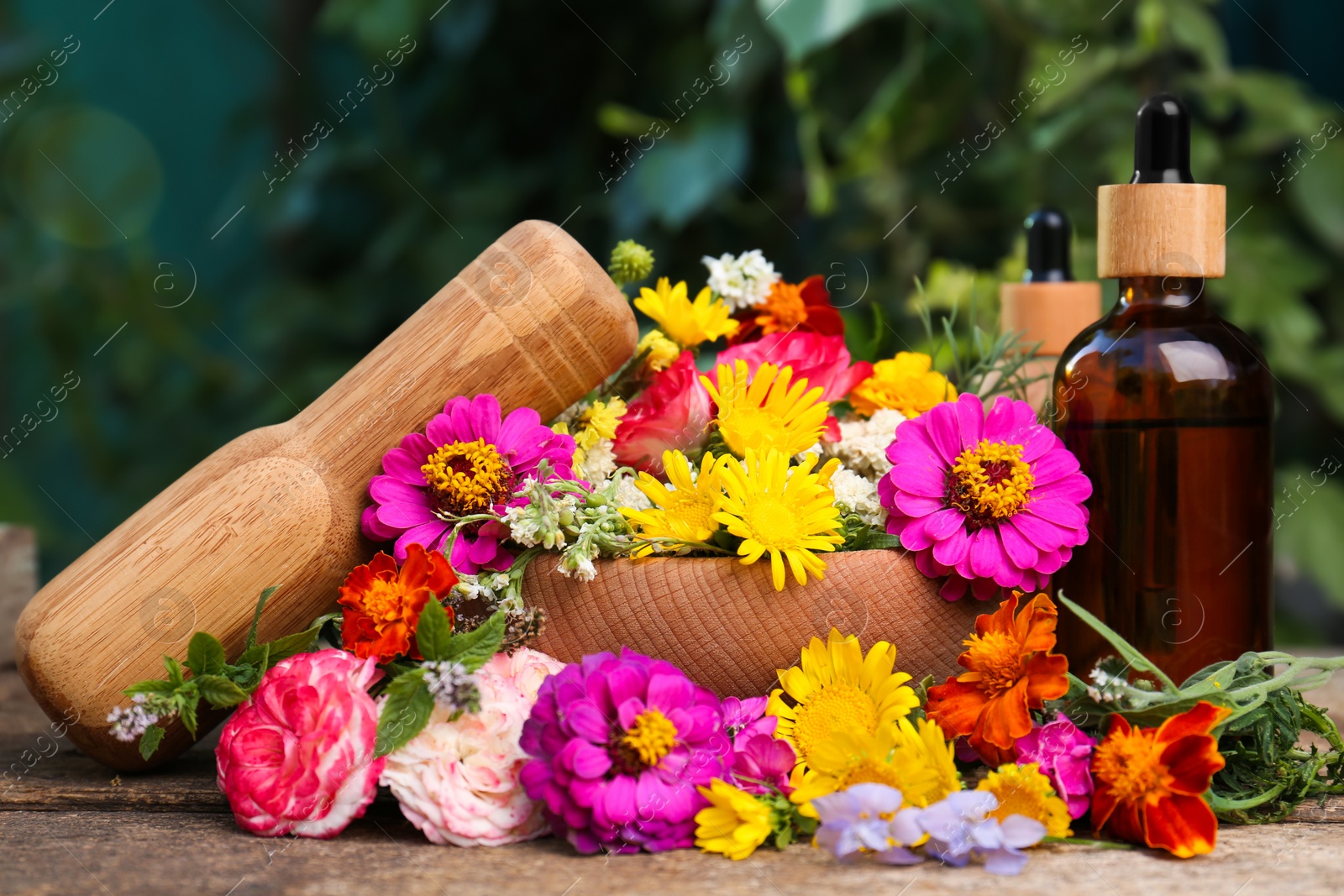 Photo of Bottles with essential oil, mortar, pestle and different flowers on wooden table outdoors
