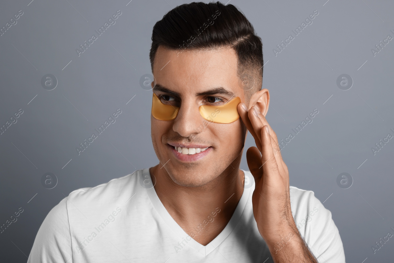 Photo of Man applying golden under eye patch on grey background