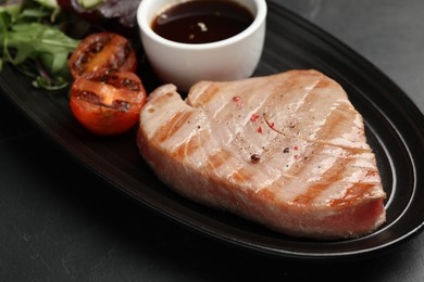 Photo of Delicious tuna steak, tomato and sauce on black table, closeup