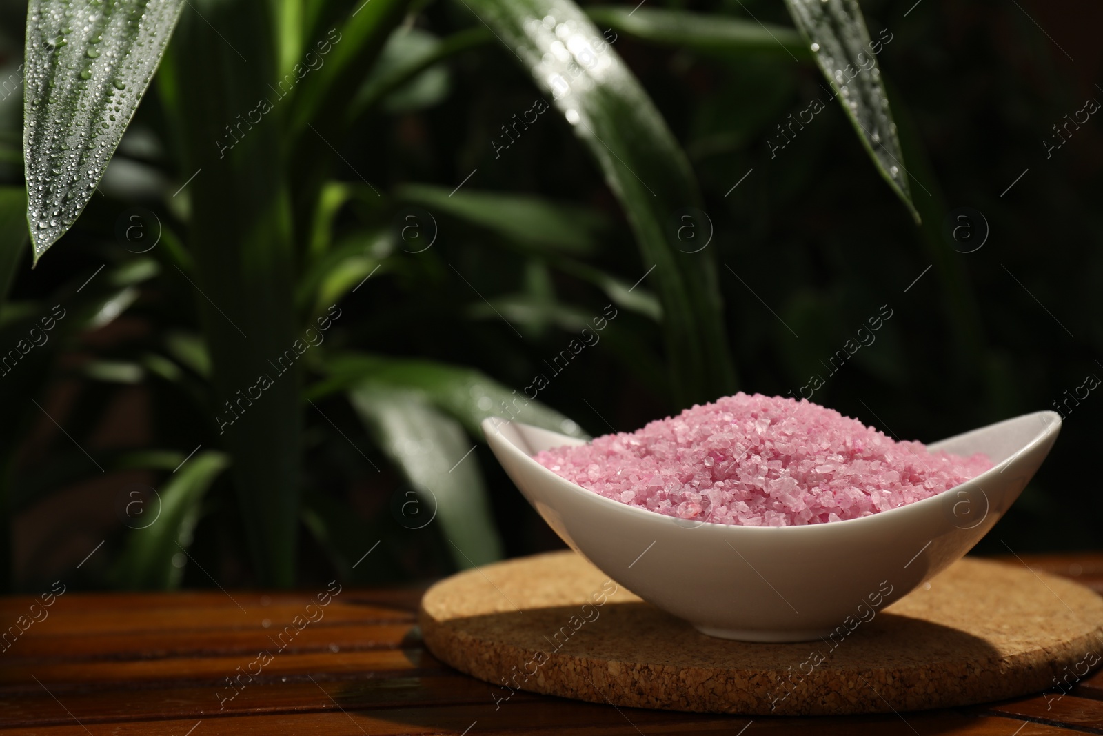 Photo of Bowl of pink sea salt on wooden table. Space for text
