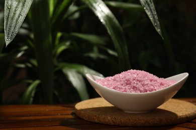 Photo of Bowl of pink sea salt on wooden table. Space for text