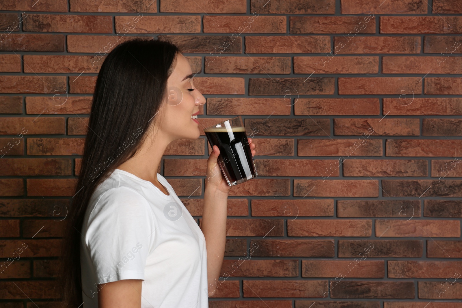 Photo of Beautiful woman with cold kvass near brick wall. Traditional Russian summer drink