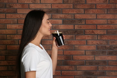 Photo of Beautiful woman with cold kvass near brick wall. Traditional Russian summer drink