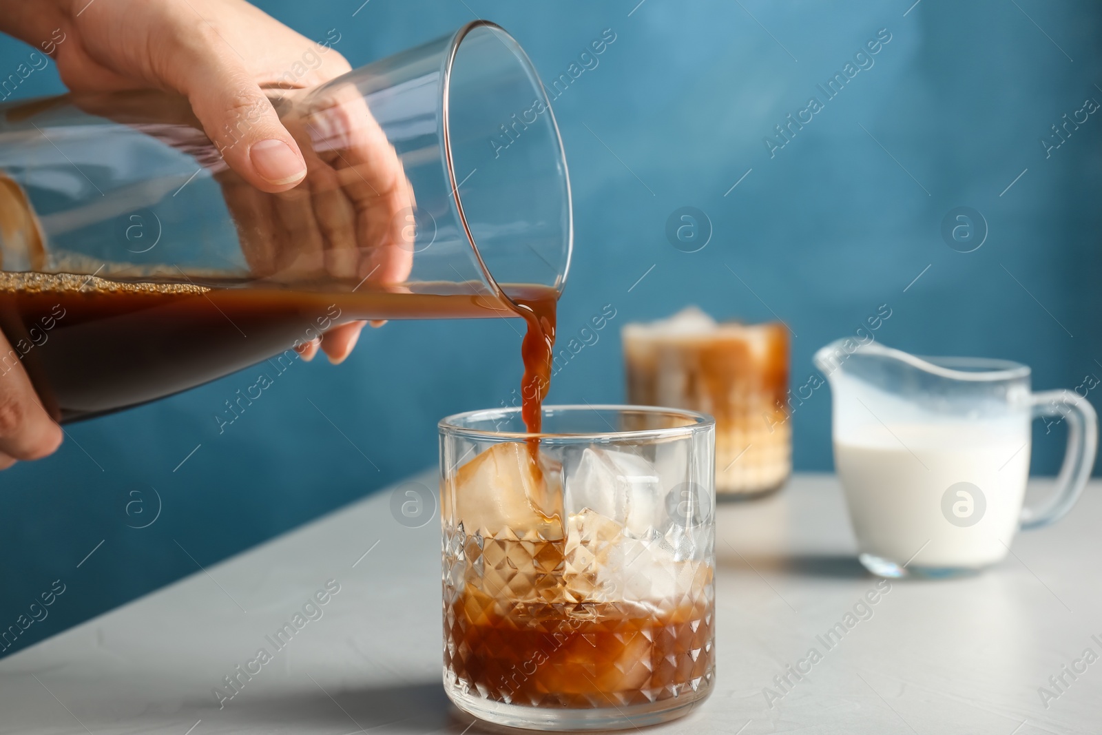 Photo of Woman pouring cold brew coffee into glass on table