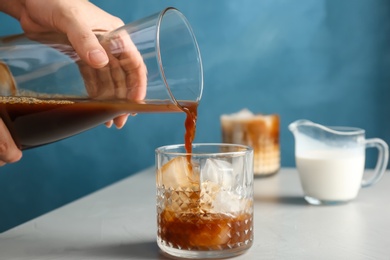 Woman pouring cold brew coffee into glass on table