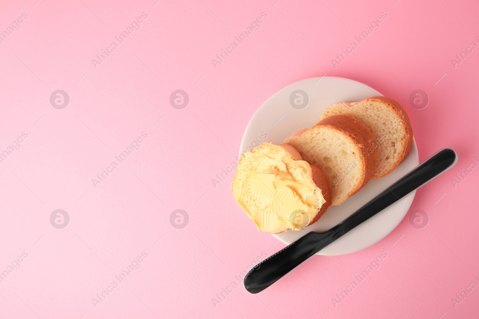 Photo of Slices of delicious baguette with butter and knife on pale pink background, top view. Space for text