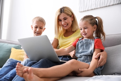 Photo of Happy mother using laptop with her children on sofa at home