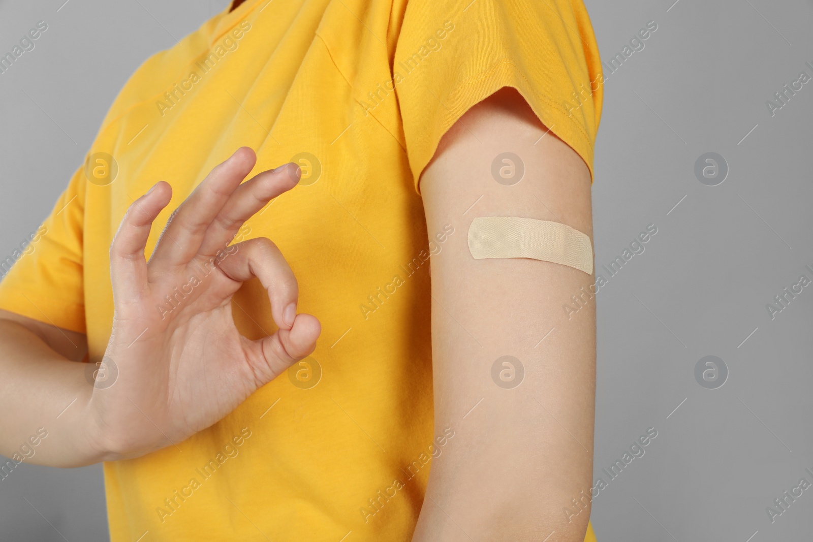 Photo of Vaccinated woman with medical plaster on her arm showing okay gesture against grey background, closeup