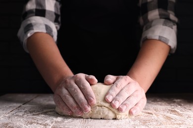 Photo of Man kneading dough at wooden table on dark background, closeup