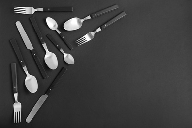 Photo of Flat lay composition with steel cutlery on black background, space for text