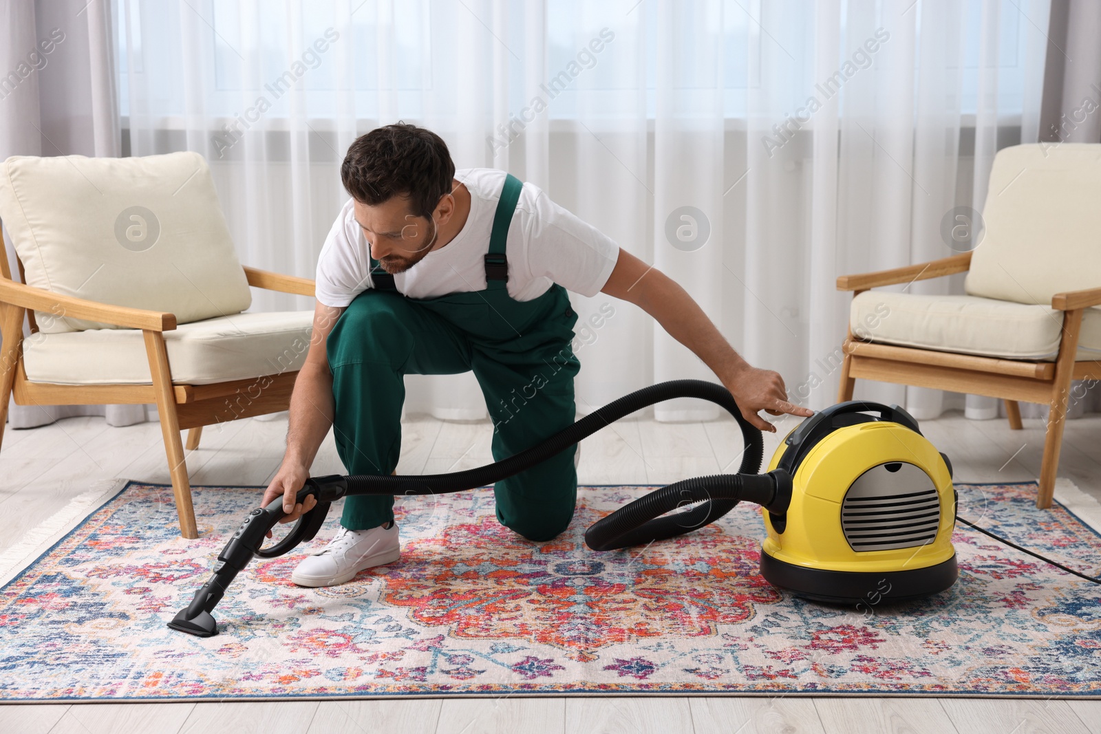 Photo of Dry cleaner's employee hoovering carpet with vacuum cleaner in room