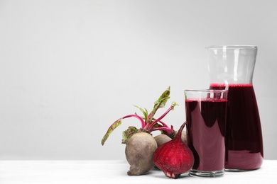 Photo of Fresh beet juice and raw vegetable on white wooden table. Space for text
