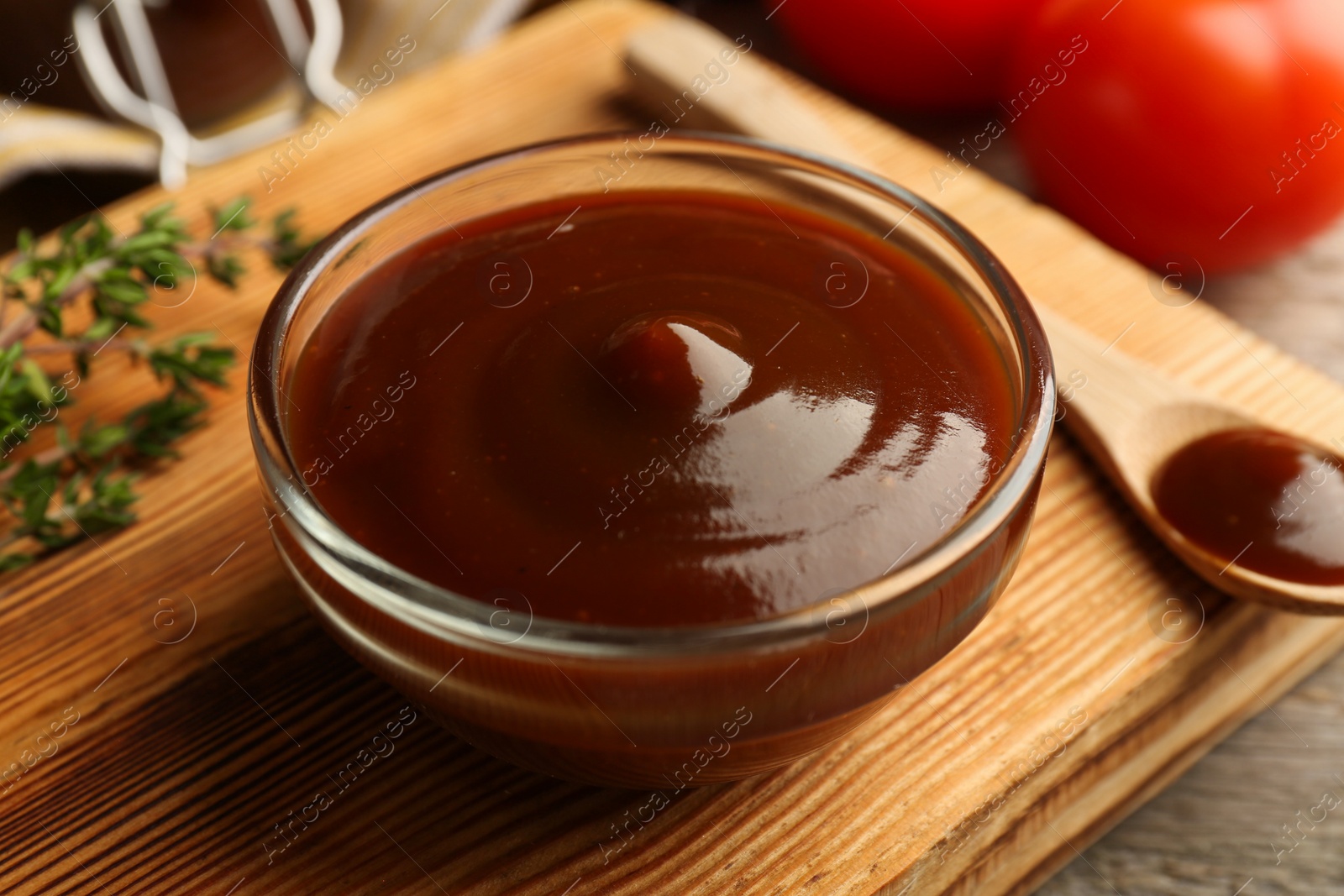 Photo of Tasty barbeque sauce in bowl and spoon on table, closeup