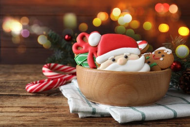 Image of Tasty decorated Christmas cookies in bowl and candy canes on wooden table. Bokeh effect