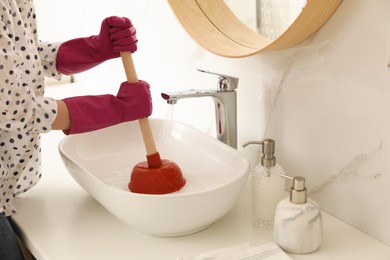 Photo of Woman using plunger to unclog sink drain in bathroom, closeup