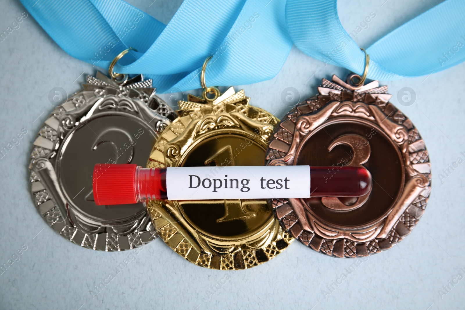 Photo of Medals and tube of blood with words Doping test on light blue background, flat lay