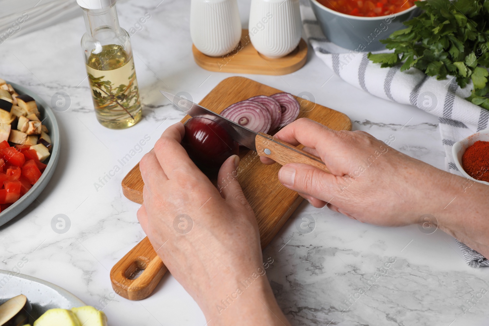 Photo of Cooking delicious ratatouille. Woman cutting fresh onion at white marble table, closeup