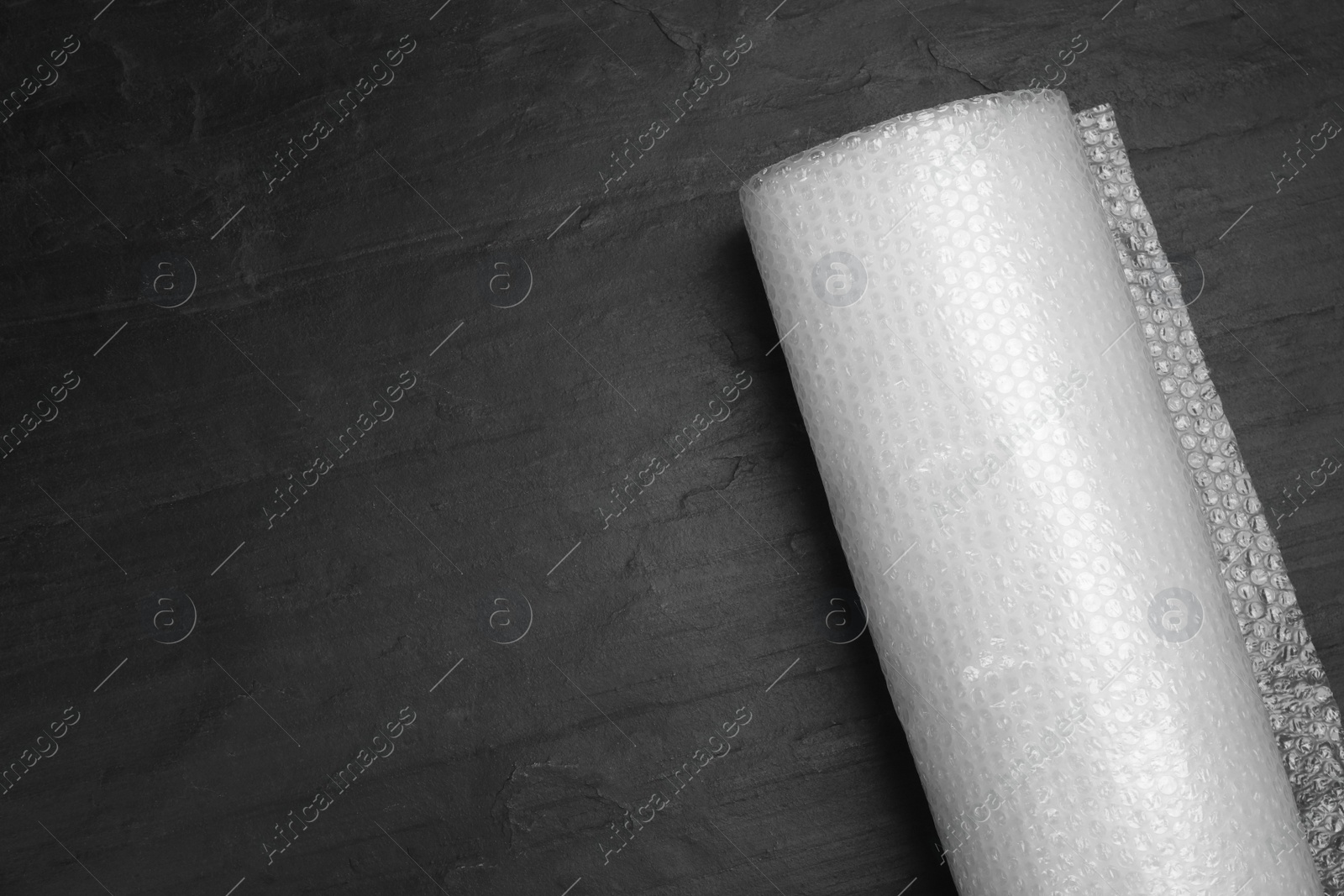 Photo of Bubble wrap roll on black background, top view. Space for text