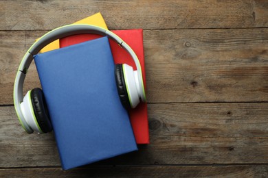 Books and modern headphones on wooden background, top view. Space for text