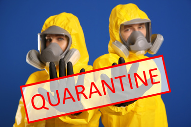 Quarantine during coronavirus outbreak. Man and woman in chemical protective suits making stop gesture against blue background