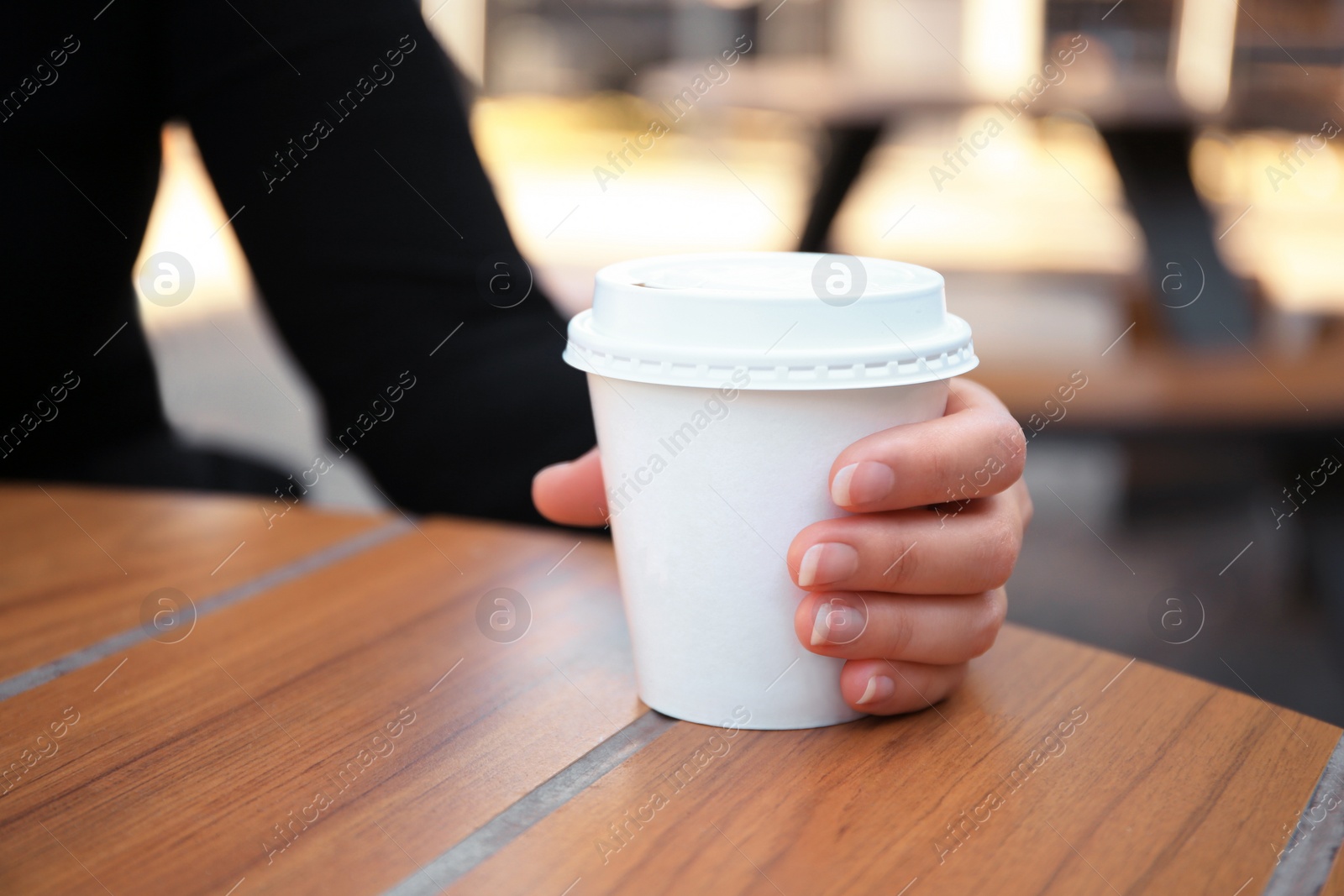 Photo of Woman with cardboard cup of coffee at table outdoors, closeup