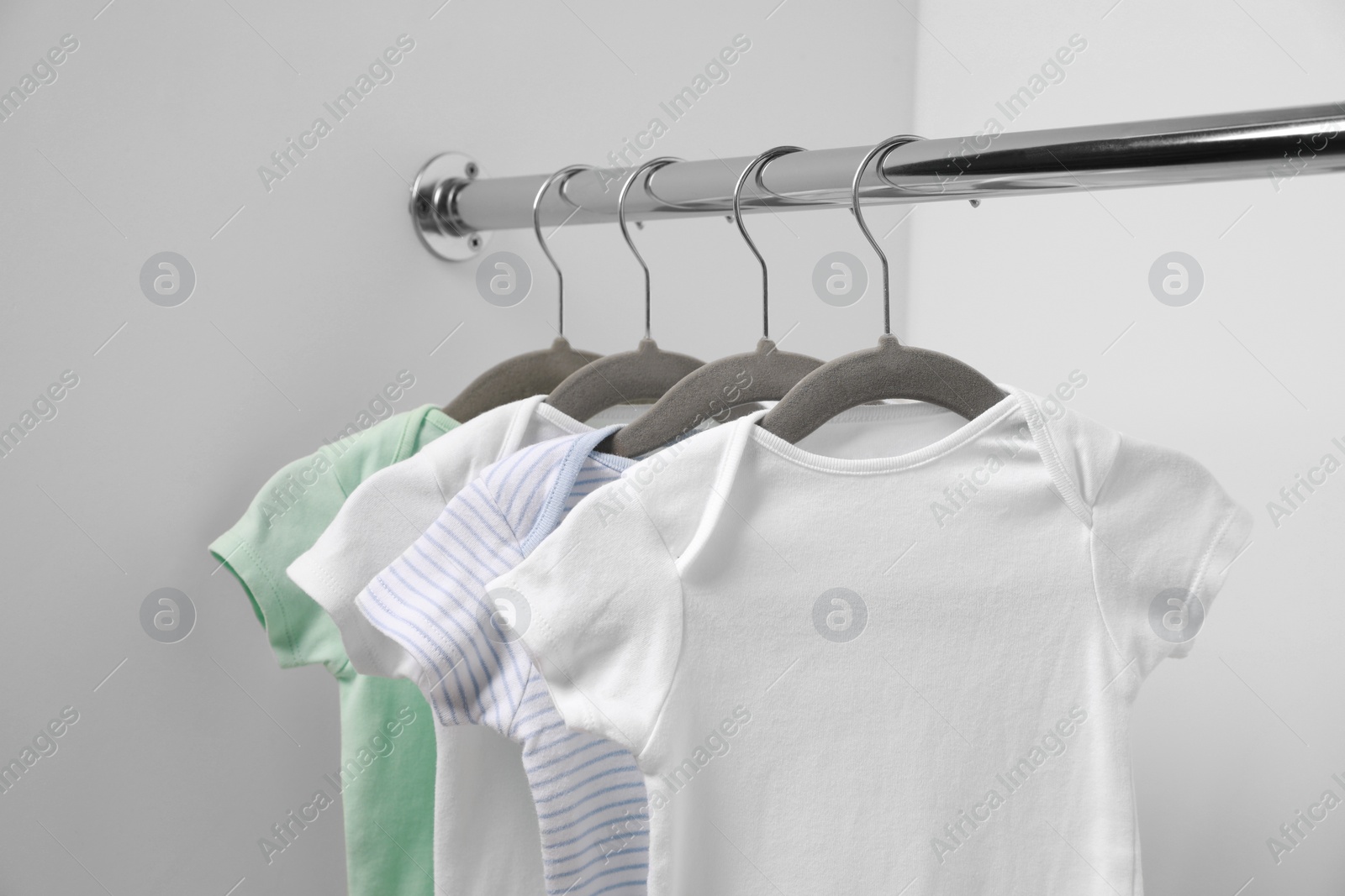 Photo of Baby bodysuits hanging on rack near white wall, closeup